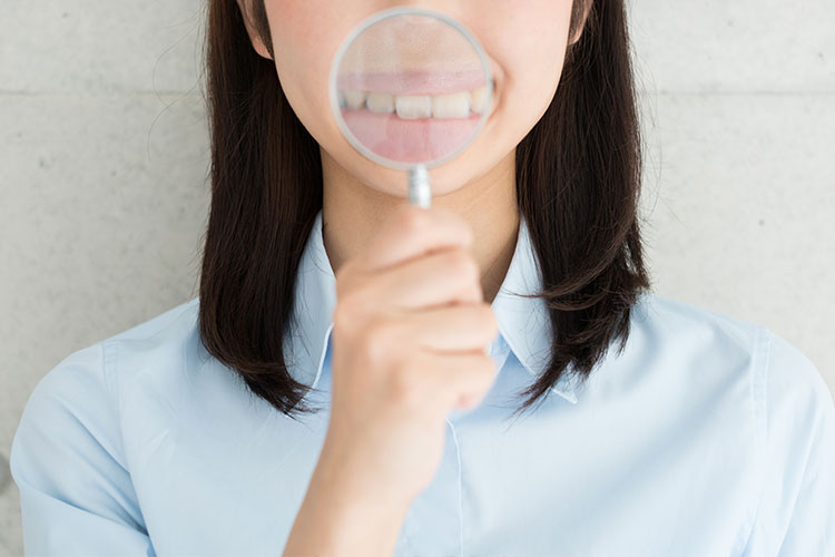 虫眼鏡で口元を拡大してみせる女性の写真